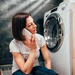 A woman talking on the phone in front of a washing machine.