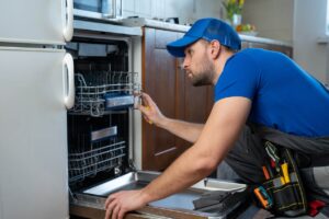 a man fixing a dishwasher in a kitchen.
