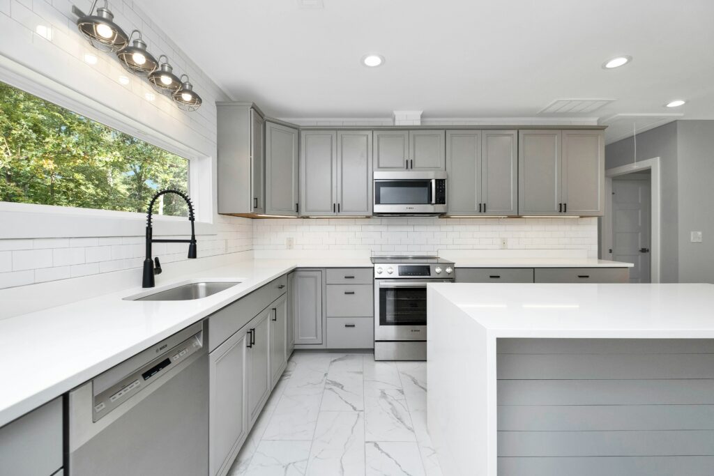 A kitchen with gray cabinets and marble counter tops.