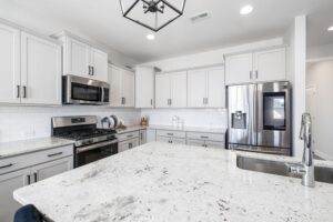 A white kitchen with granite counter tops and stainless steel appliances.