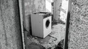 A black and white photo of a washing machine in an abandoned building.