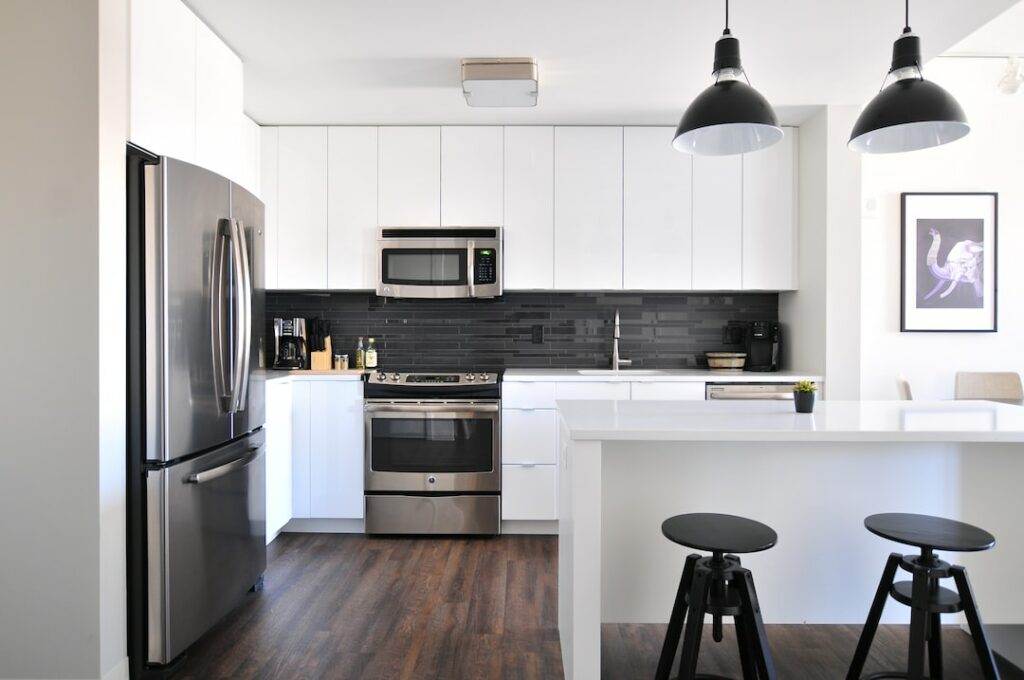 Modern kitchen with sleek stainless steel appliances, including a refrigerator, oven, and microwave, complemented by a black backsplash and white cabinets, representing stylish and efficient home appliance repairs.