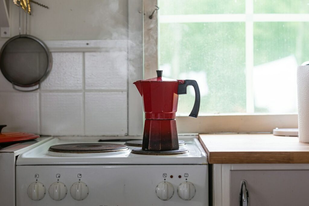 a red coffee pot on top of a stove in a kitchen.