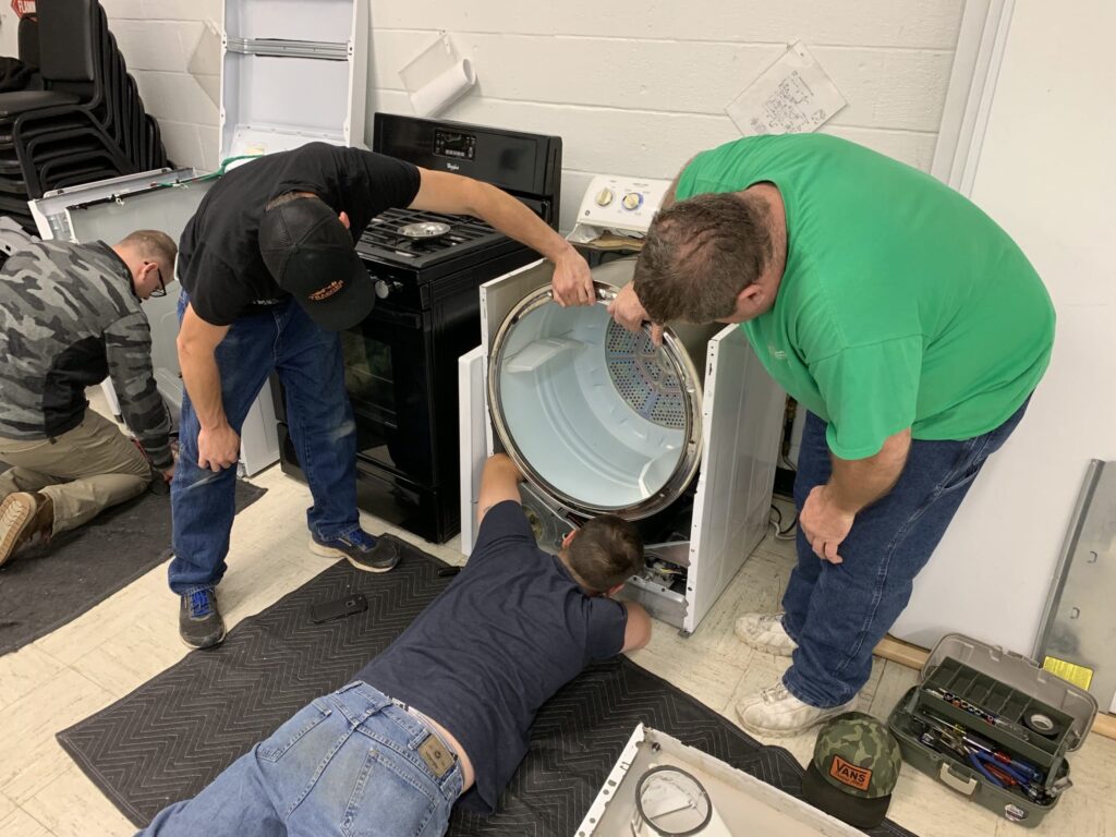 Technicians repairing a dryer in a workshop setting, showcasing affordable appliance repair services.